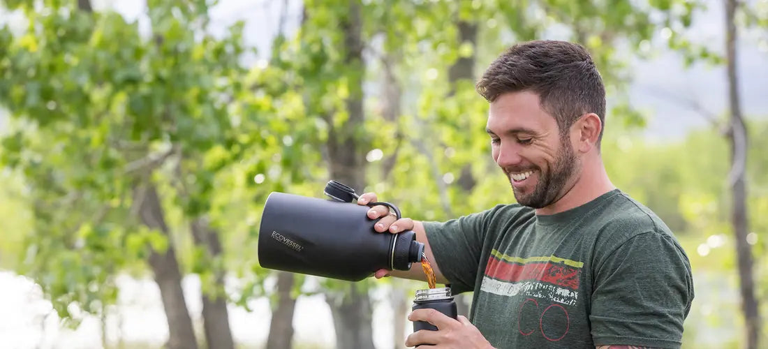 A smiling man pouring from a black EcoVessel BOSS growler into a PERK travel mug among green trees