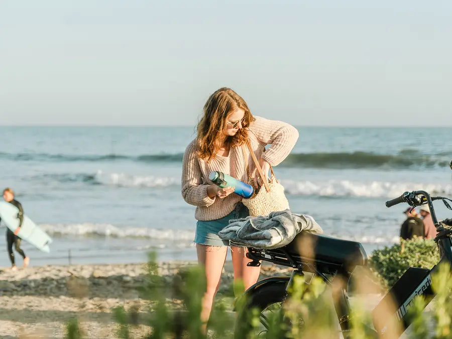 A woman on a beach path in the morning sun with her teal EcoVessel bottle