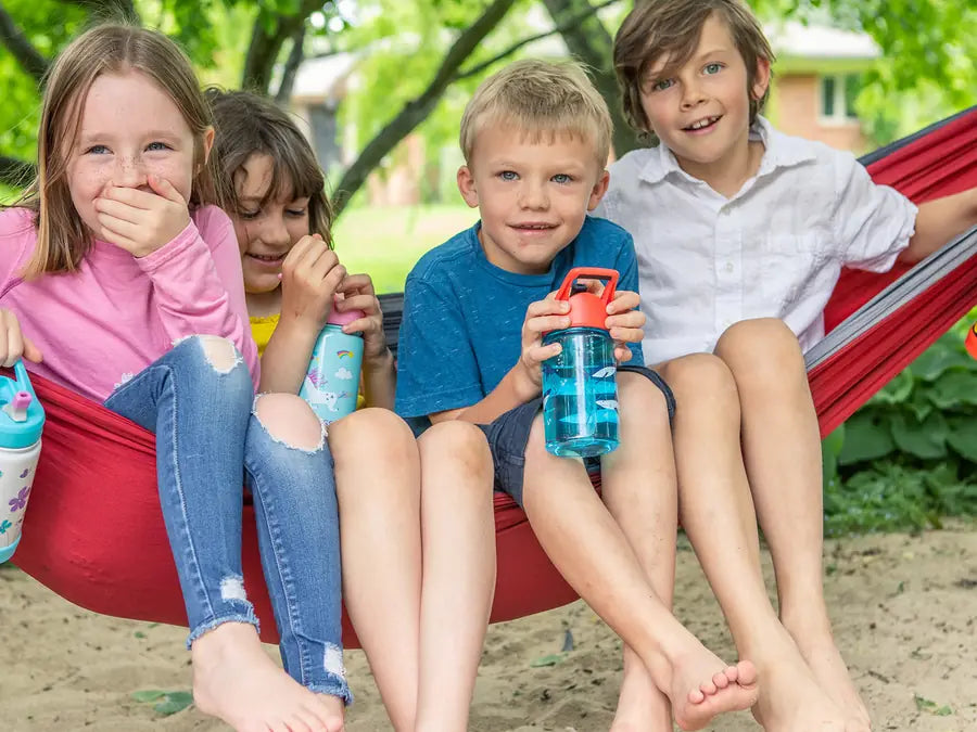 Four kids laughing in a red hammock, holding their EcoVessel kids bottles