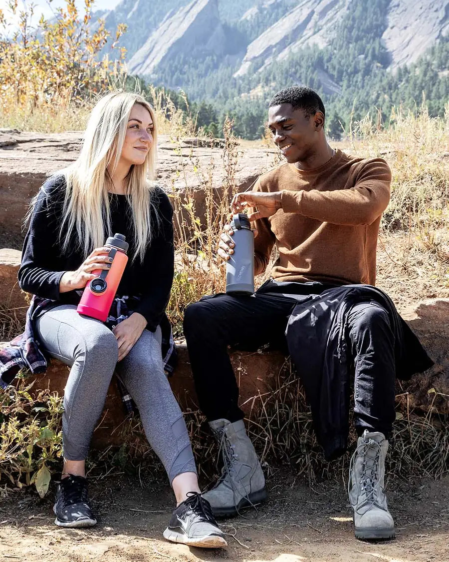 Two hikers resting on a mountain trail with their EcoVessel Boulder bottles